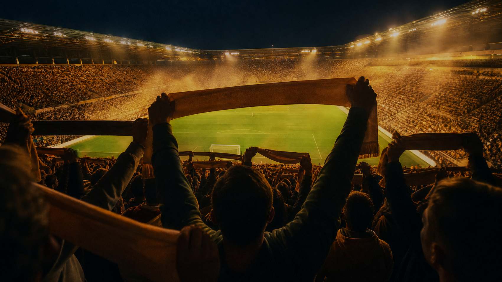 Dicht besetzte Kurve bei Flutlicht, Fans von hinten mit erhobenen Schals